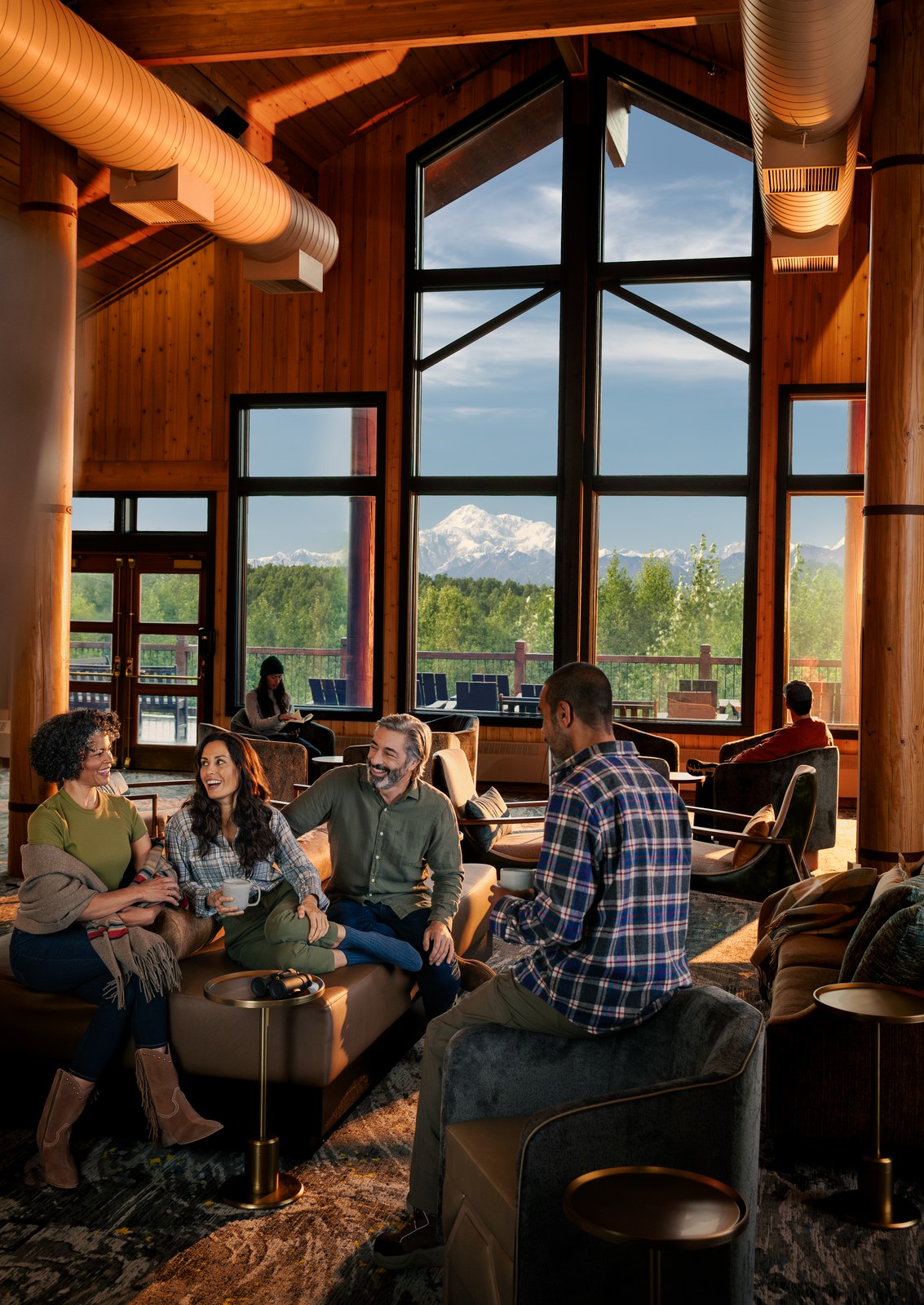 Alaska 2024 land-tour photography: guests in the great room at McKinley Princess Wilderness Lodge, Denali through the windows