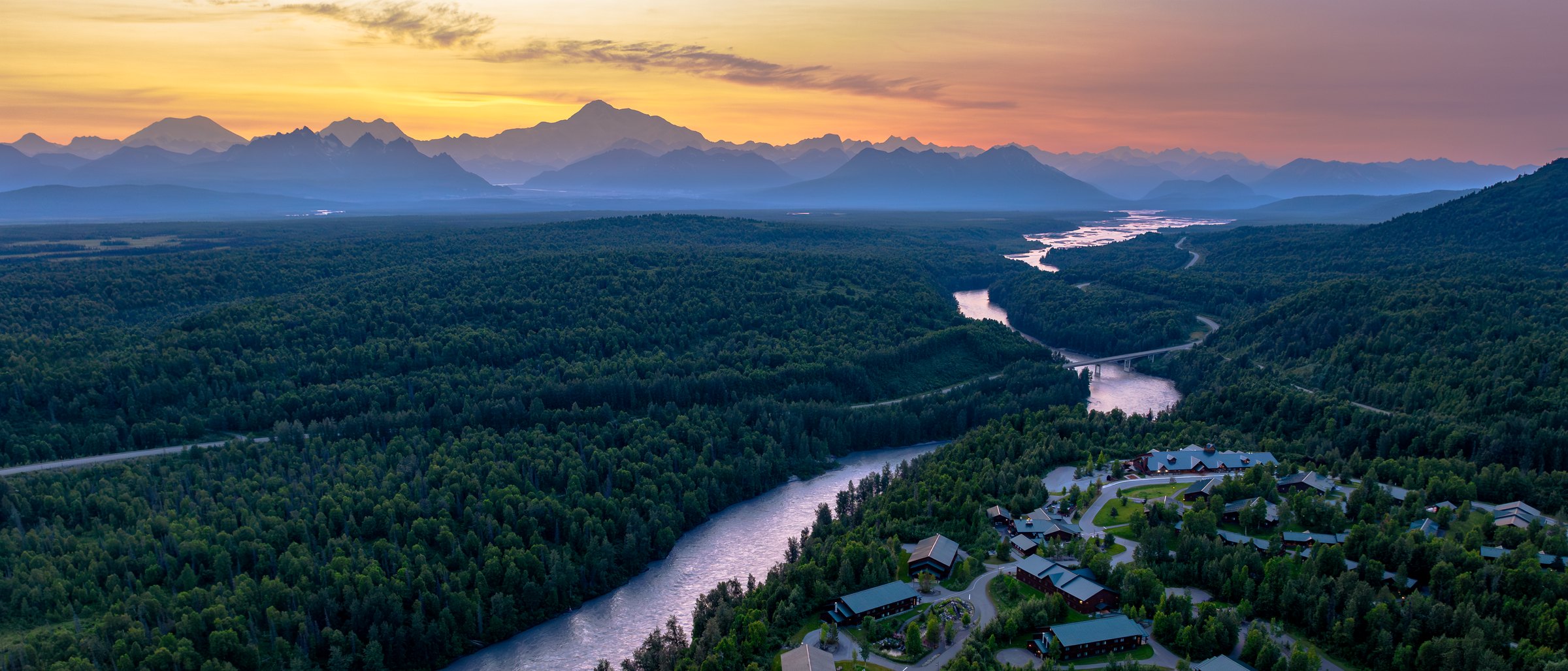 McKinley Princess Wilderness Lodge at sunset above the river, with Denali on the horizon